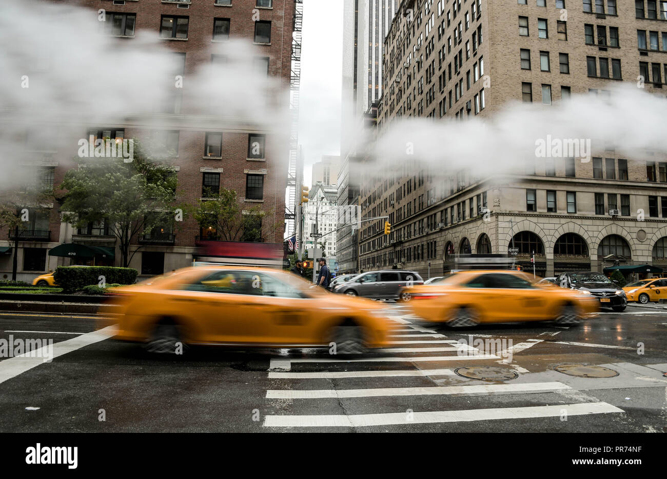 Rouleau de taxis dans un tableau comparatif à l'angle de Park Avenue et de la 57e Rue à New York City par une matinée pluvieuse que la vapeur d'un vent souffle par. Banque D'Images
