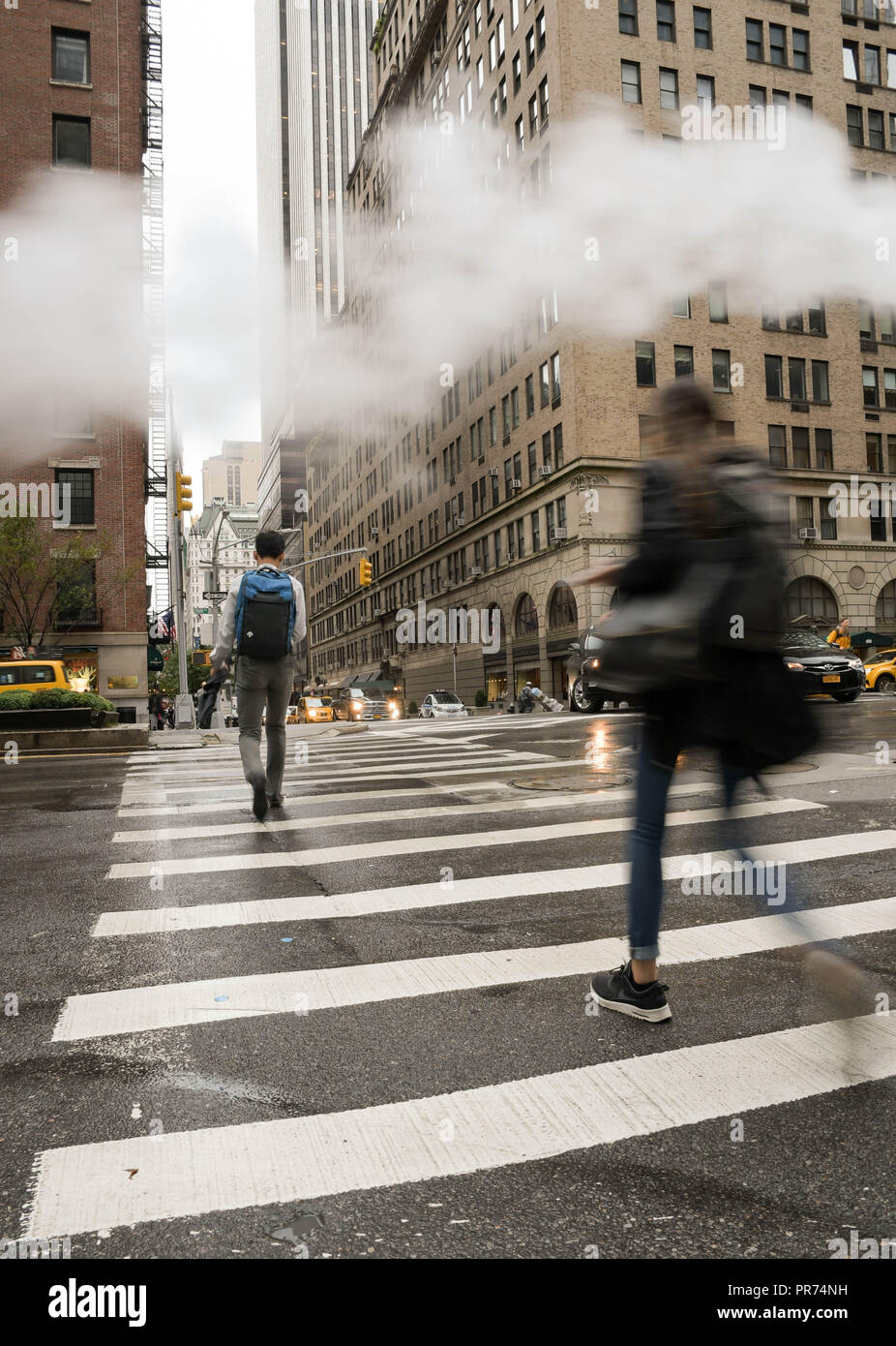 Les piétons utiliser un passage pour piétons à l'intersection de l'avenue Park et East 57th Street sur une matinée pluvieuse dans la ville de New York. Banque D'Images