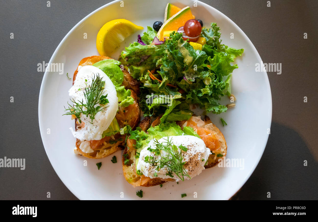Oeufs Royale, oeufs pochés au saumon fumé gravlax () et d'avocat avec un mélange de salade de fruits frais and​ sur une plaque blanche Banque D'Images