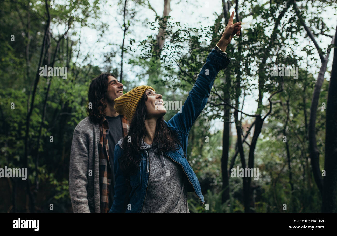 Jeune couple en forêt, avec femme pointant vers le haut et de sourire. Heureux l'homme et la femme à la recherche de quelque chose d'intéressant dans la forêt. Banque D'Images