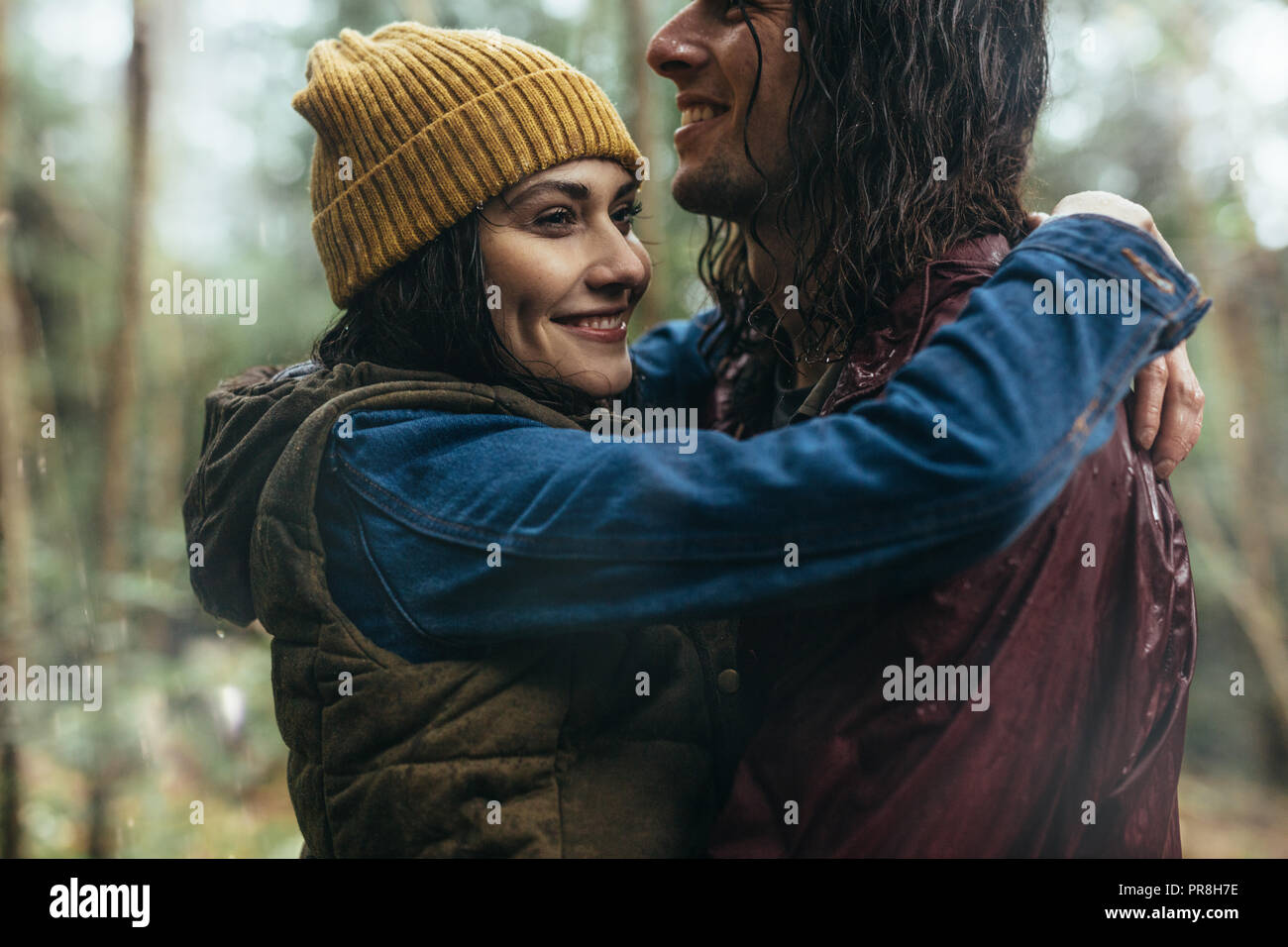 Belle femme embrassant son petit ami sous la pluie à l'extérieur. Couple wearing imperméables au parc se mouiller sous la pluie. Banque D'Images