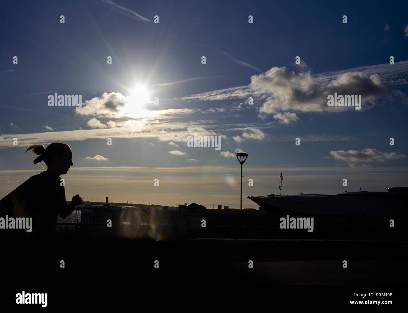 Jogger passé en courant avec soleil directement derrière Liverpool Pier Head Banque D'Images