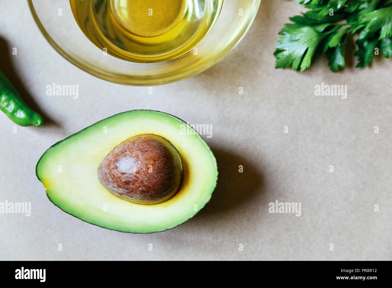 La moitié de l'avocat à des semences avec de l'huile servi dans un verre au-dessus sur fond brun neutre Banque D'Images