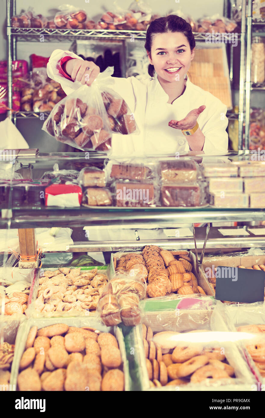 Young smiling saleswoman posant avec cookies au compteur dans sweets shop Banque D'Images