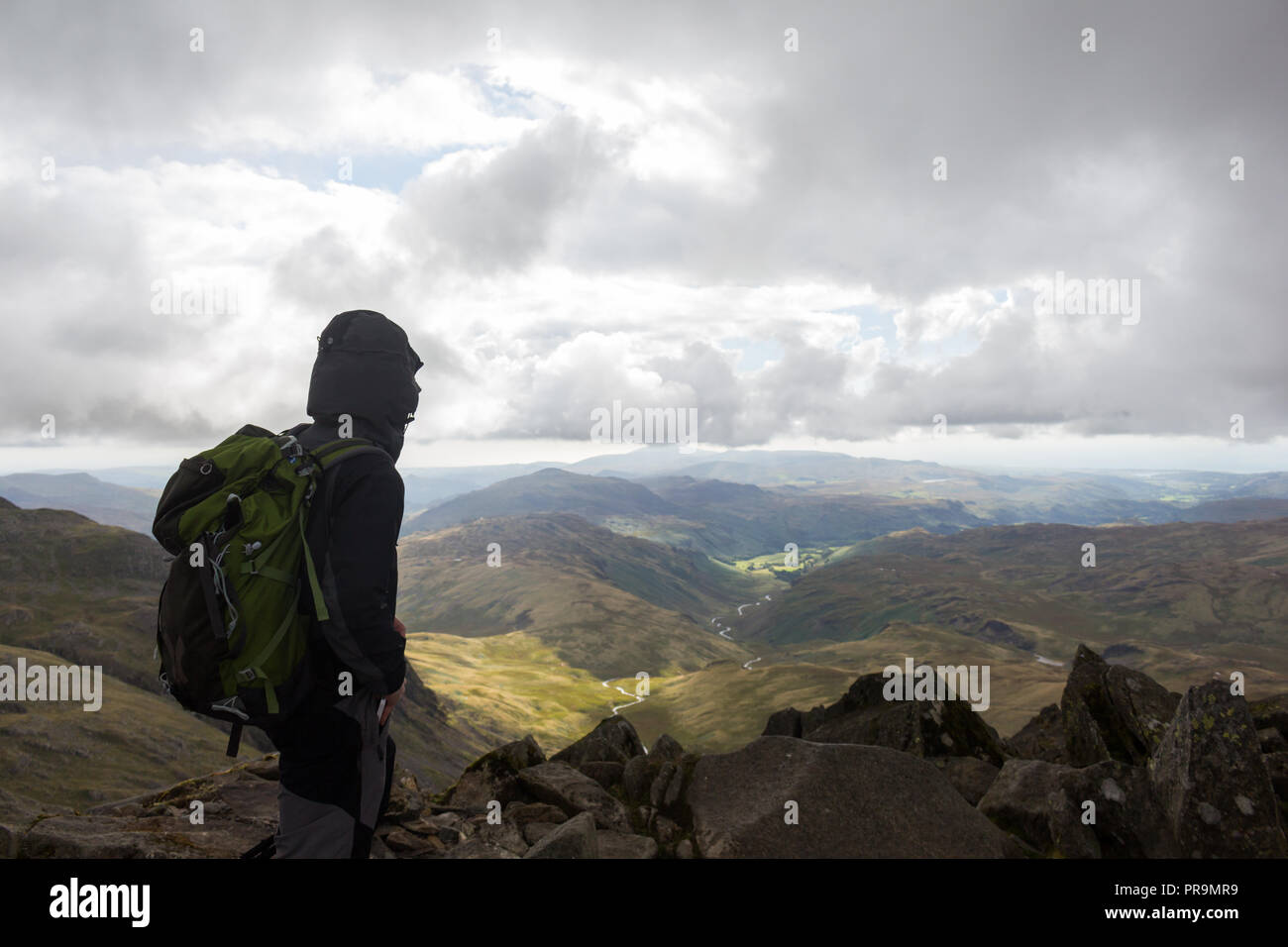 Un hillwalker profitant de la vue depuis le sommet du Bowfell à vers Hard Knott sur un coudy jour dans le Lake District, Cumbria, Angleterre. Banque D'Images