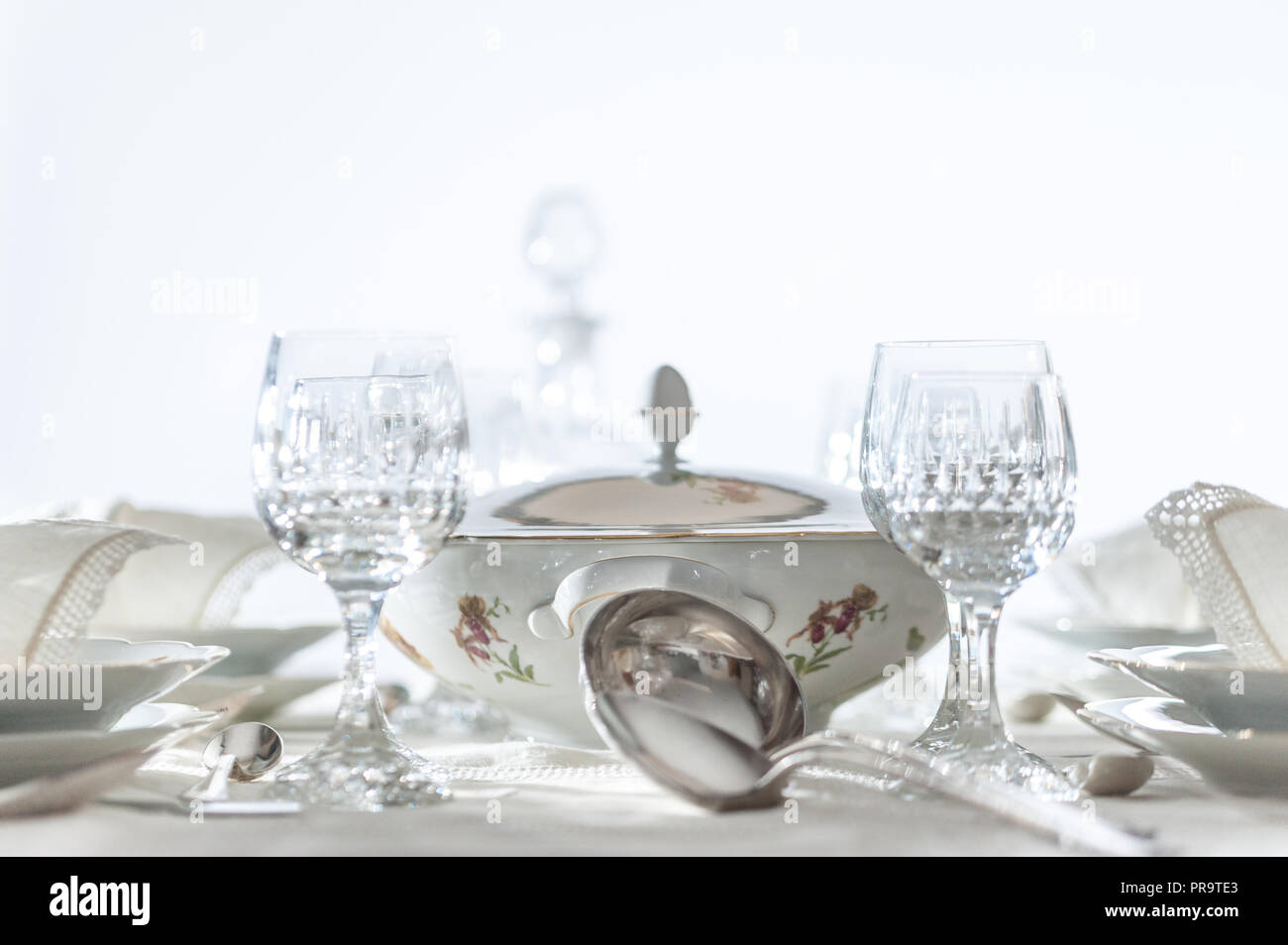 Manger amende : blanc motif floral de Chine dîner organisé sur une table avec nappe vintage et napikins, verres en cristal. Focus sélectif. Banque D'Images