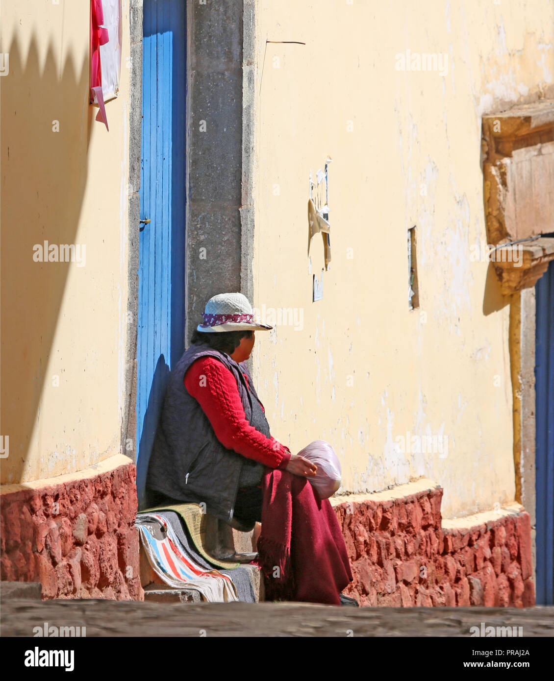Femme assise sur les marches de sa maison le long de rue avec des murs en plâtre et en pierre Banque D'Images