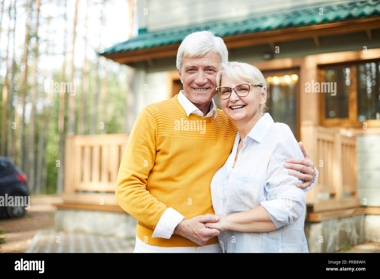 Maison Forestière des grands-parents : happy senior couple embracing excités les uns les autres et de rire tout en regardant la caméra et se tenir contre cottage Banque D'Images