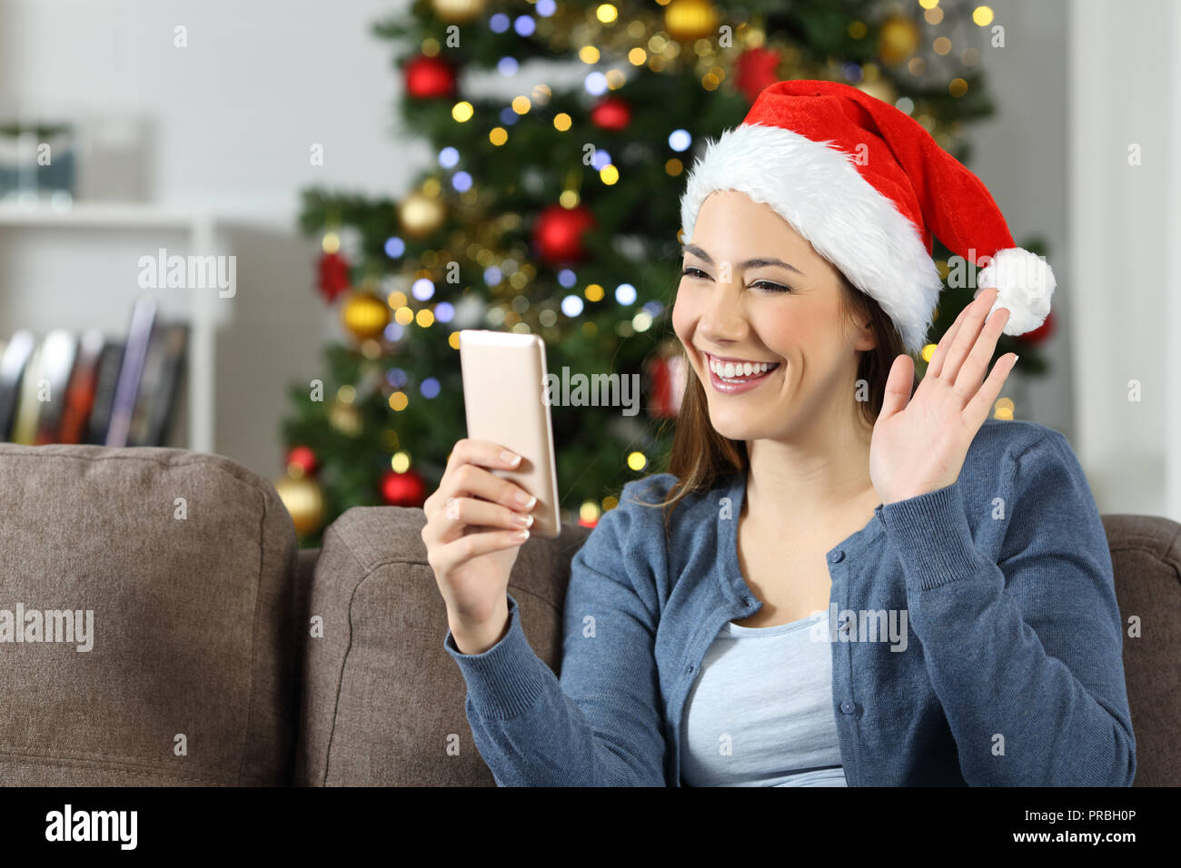 Woman waving pendant un appel vidéo smart phone in christmas assis sur un canapé dans la salle de séjour à la maison Banque D'Images