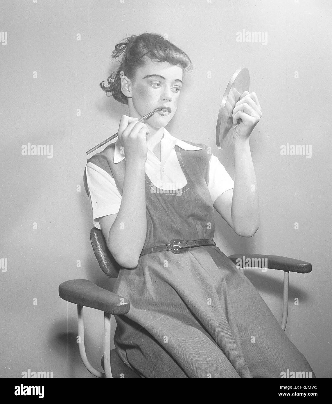 Femme dans les 1950s. Une jeune actrice se moque et met sur le maquillage théâtral en se regardant dans le reflet d'un couvercle de pot. Suède 1952. Photo Kristoffersson réf. BD90-9 Banque D'Images