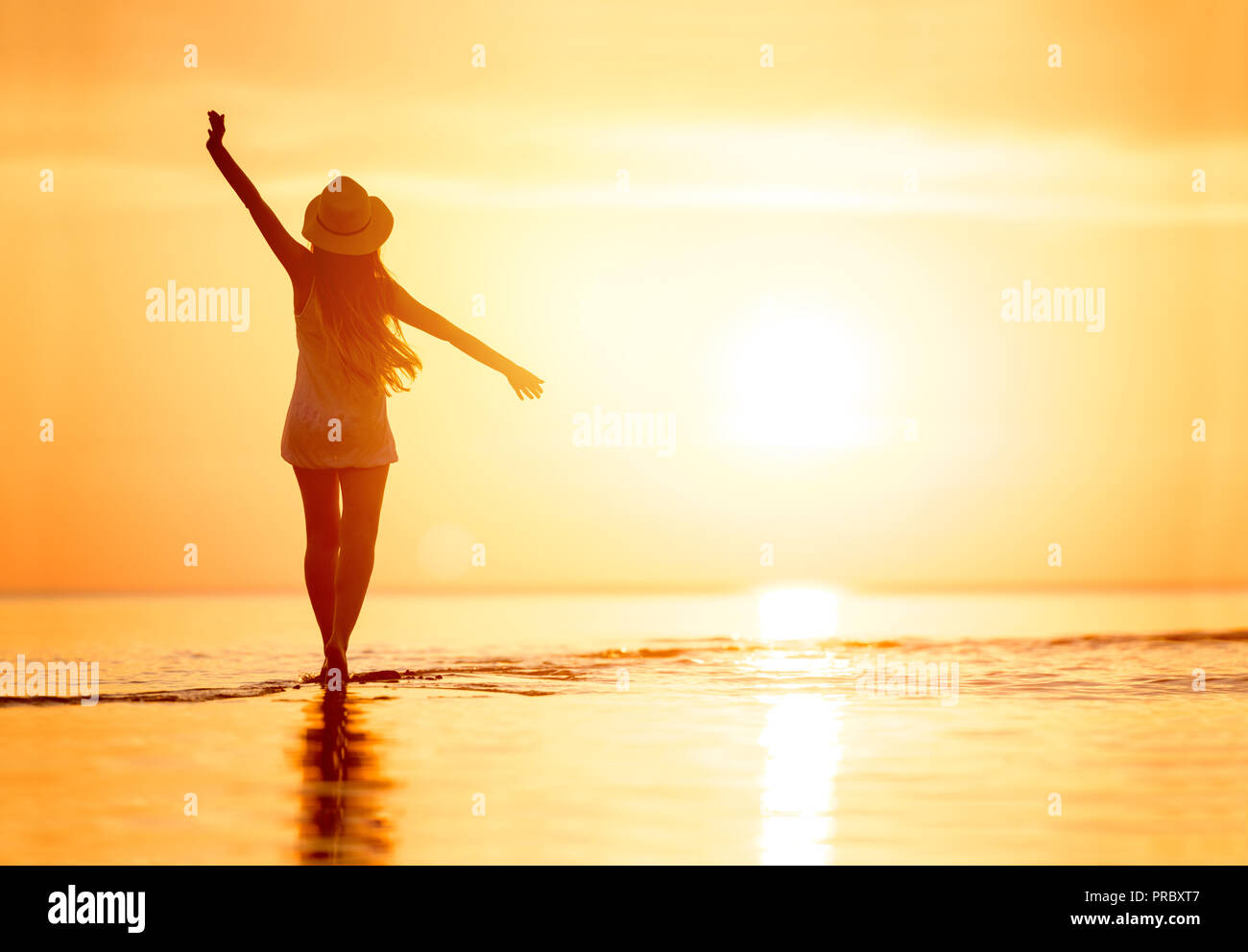 Silhouette de femme avec bras levés contre calme Plage de Sunset Banque D'Images