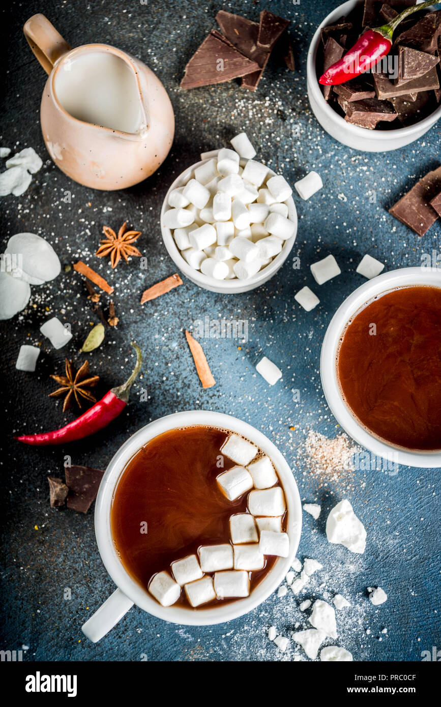 Tasses de chocolat chaud, morceaux de chocolat, sucre, guimauve, piment rouge et d'épices. Arrière-plan de béton bleu foncé top view space Banque D'Images