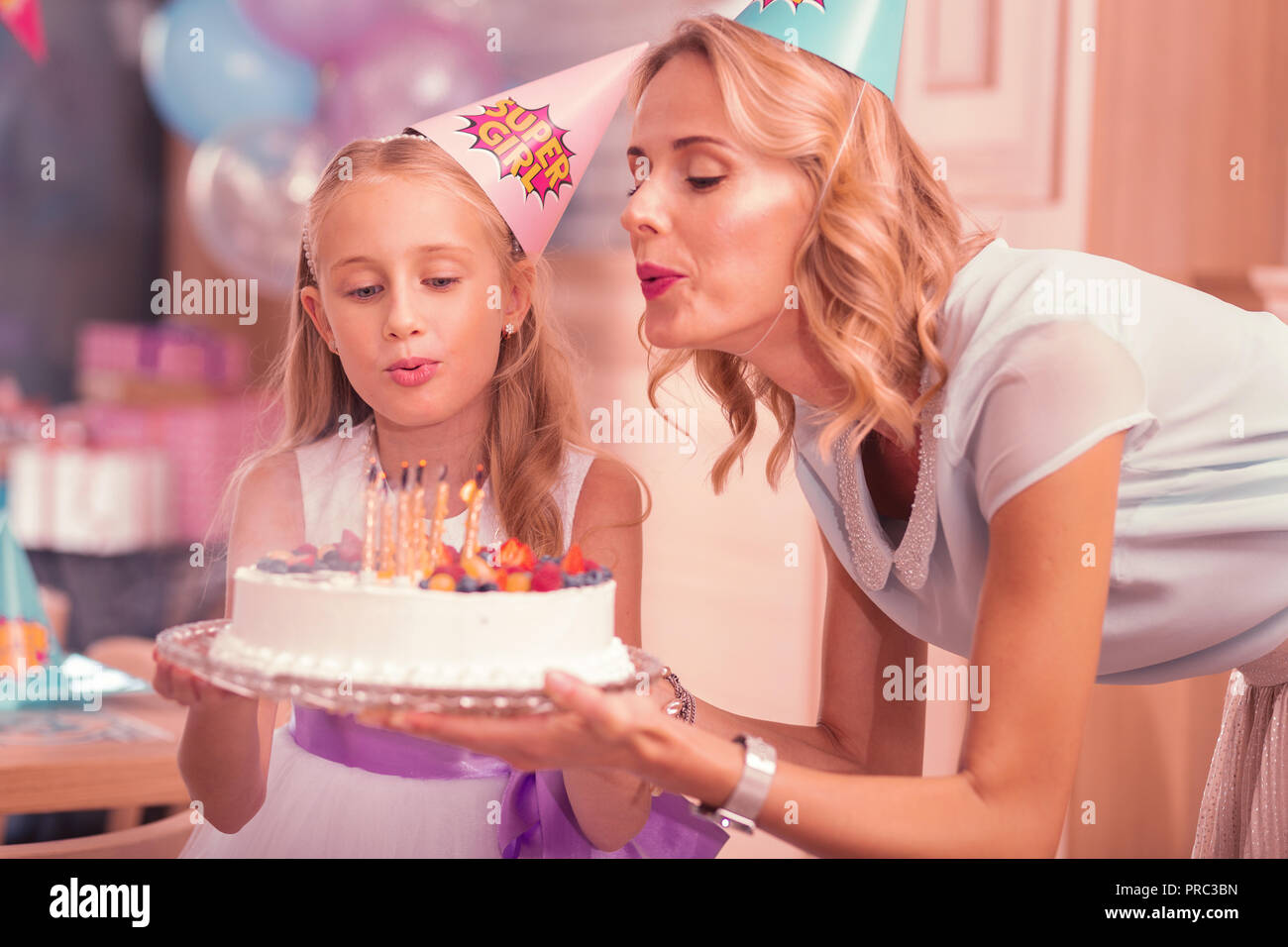 Jeune femme et sa fille soufflant des bougies sur le gâteau d'anniversaire Banque D'Images