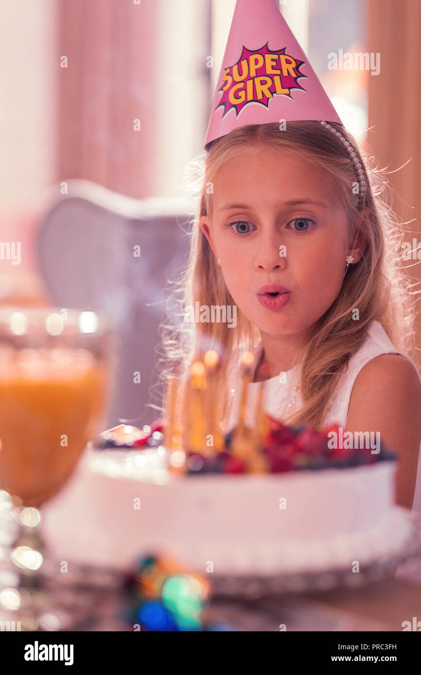 Cute girl blowing anniversaire les bougies et se sentir impressionné par son cake Banque D'Images
