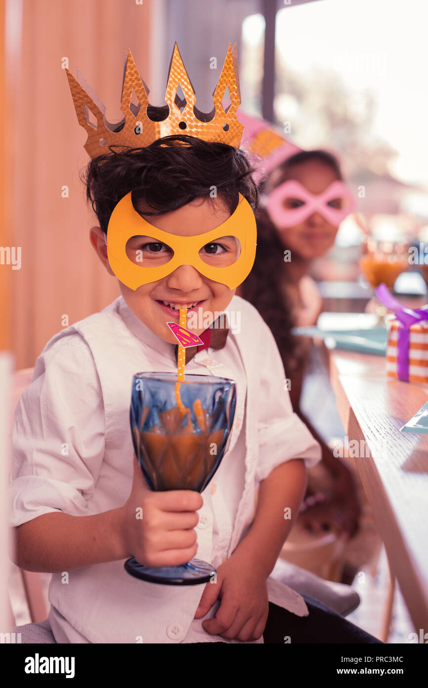 Funny boy wearing mask et souriant alors que boire du jus Banque D'Images