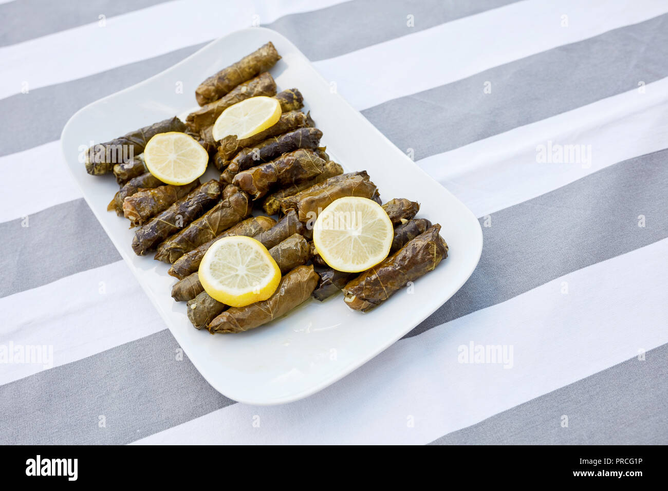 Feuilles de vigne farcies avec de l'huile d'olive et de tranches de citron servi dans une assiette de porcelaine blanche sur une nappe à rayures. Yaprak dolmasi Zeytinyagli. Banque D'Images