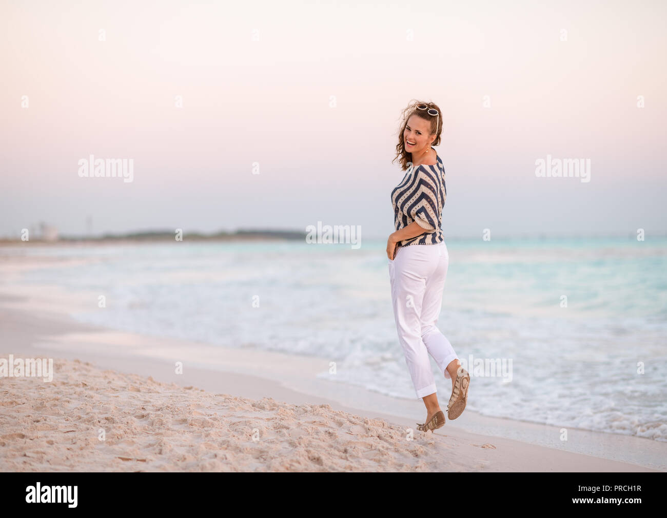 Portrait de femme moderne dans un pantalon blanc et chemise rayée sur le bord de la mer au coucher du soleil Randonnée pédestre Banque D'Images