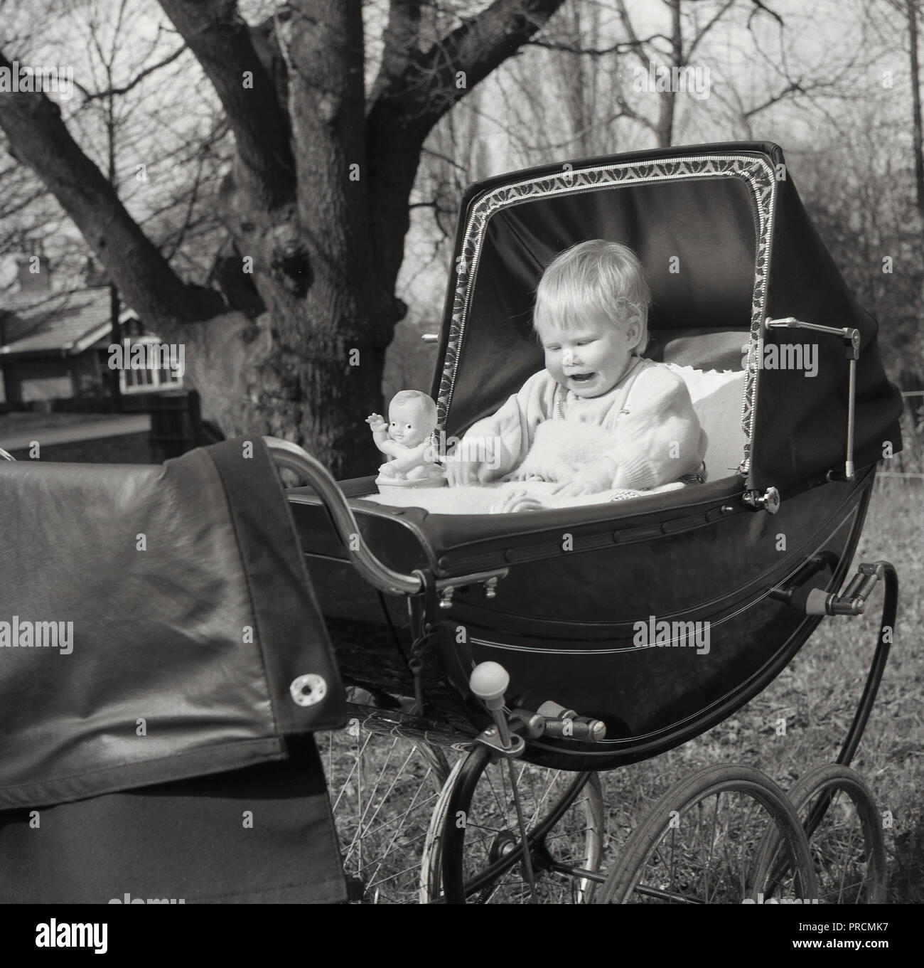 Années 1950, historiques, heureux bébé, un garçon (enfant) assis bien droit dans un landau capucines ou la pram avec capot, avec son jouet figure à côté de lui, en Angleterre, UK. Banque D'Images