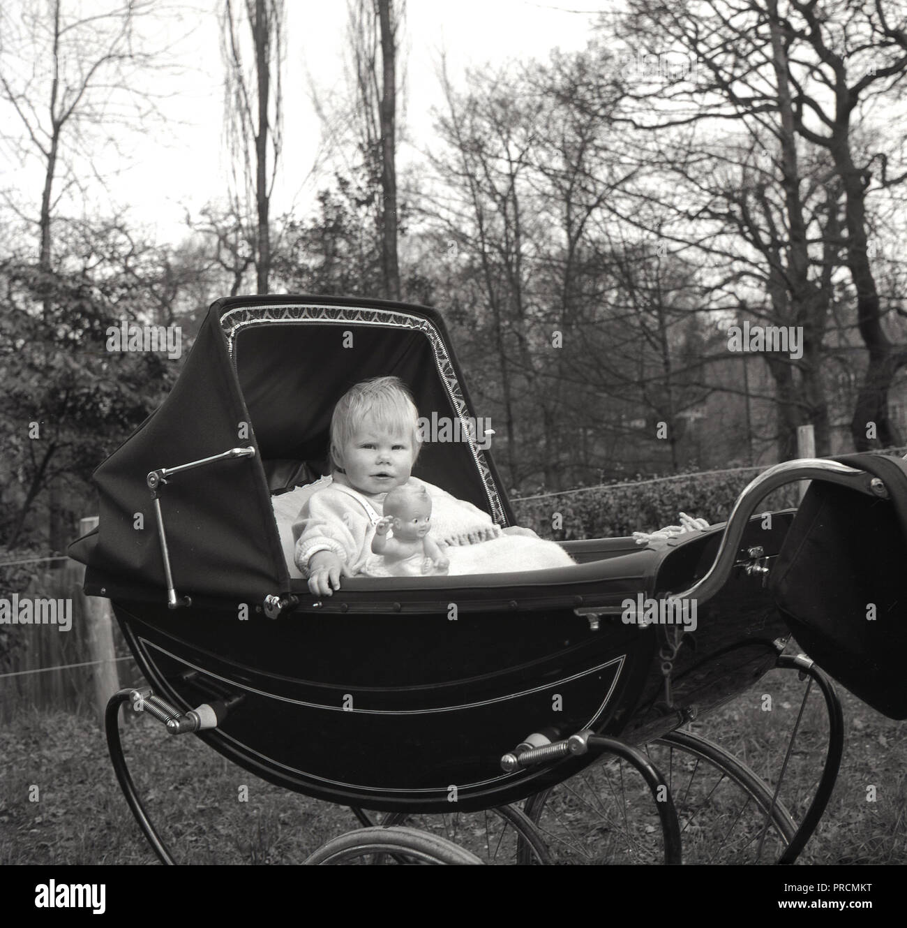 Années 1950, historiques, jeune enfant, un garçon (enfant) assis bien droit dans un landau capucines ou la pram avec capot, avec son jouet figure à côté de lui, en Angleterre, UK. Banque D'Images