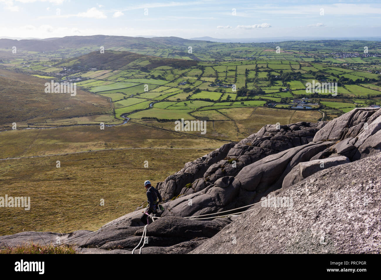 Un varappeur expérimenté les apprenants de l'assurage du haut d'un rocher de la montagne montagnes de Mourne en poule, N.Ireland. Banque D'Images