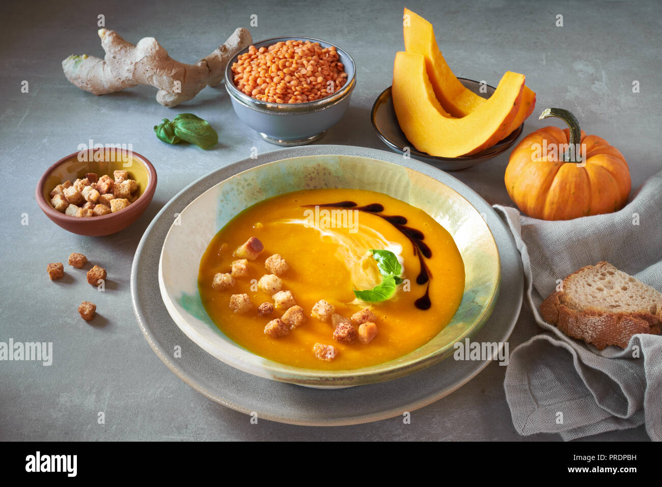 Crème de lentilles rouges et de Citrouille en soupière et Bol en céramique assaisonnée de basilic, crème et croûtons. Tranches de citrouille, les lentilles, le gingembre et l'assaisonnement autour Banque D'Images