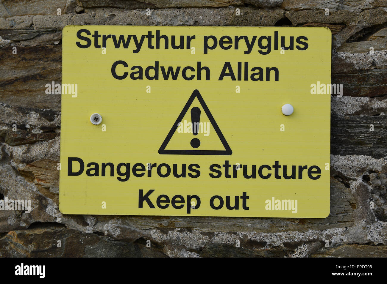 Gallois structure dangereux Strwythur peryglus Cadwch Tenir hors Allan signe avec le texte noir sur fond jaune d'exclamation avec vieux mur de pierre Banque D'Images