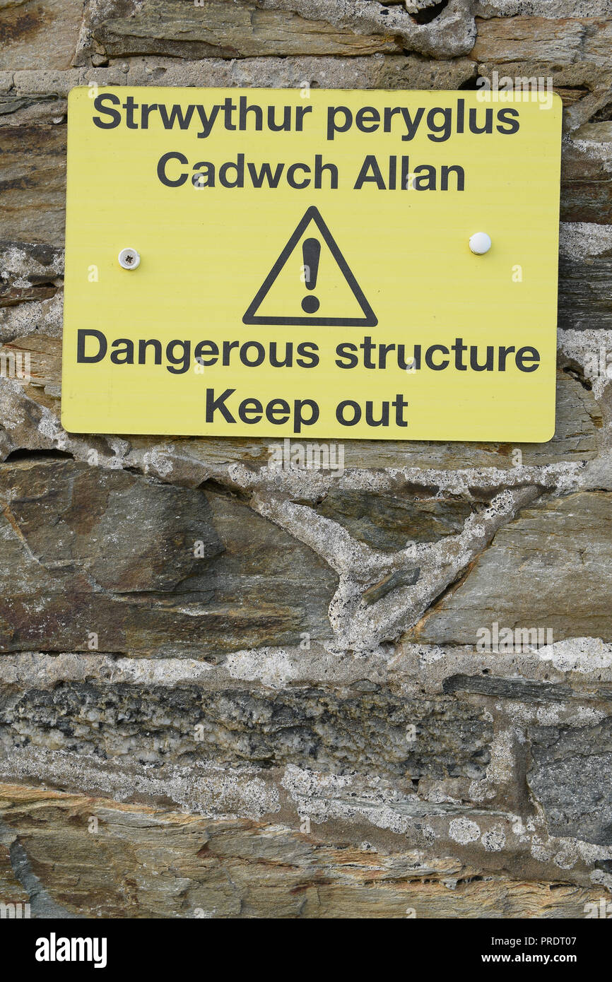 Gallois structure dangereux Strwythur peryglus Cadwch Tenir hors Allan signe avec le texte noir sur fond jaune d'exclamation avec vieux mur de pierre Banque D'Images