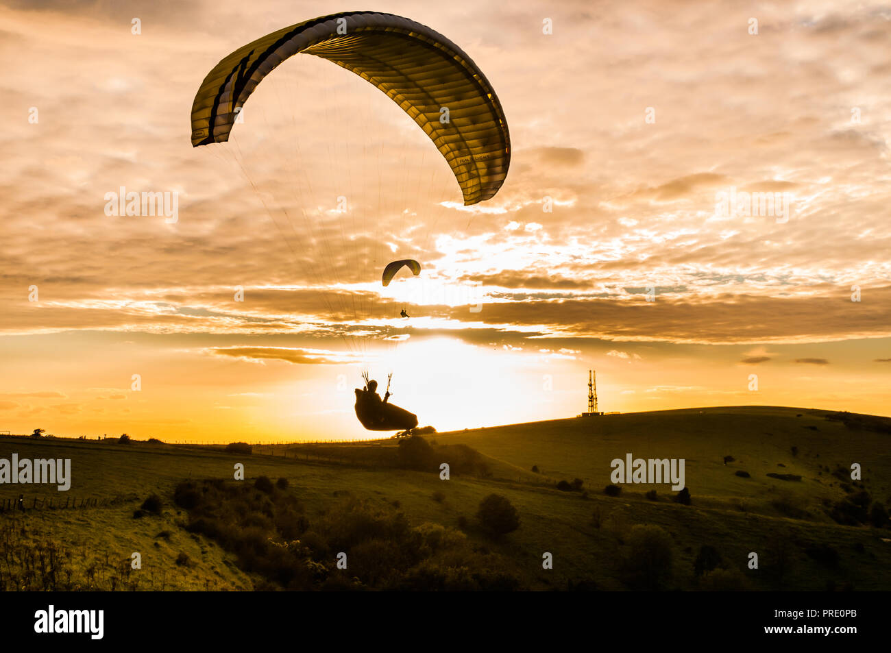 Firle Beacon, Lewes, East Sussex, Royaume-Uni. 1 octobre 2018..Paragliders silhouetted contre le soleil sous la couverture nuageuse d'Altocumulus. Le vol sur le site des South Downs n'a été possible que pendant une courte période autour du coucher du soleil, car le vent fort de rafales du Nord-Ouest calmé à des conditions de vol sûres. Banque D'Images