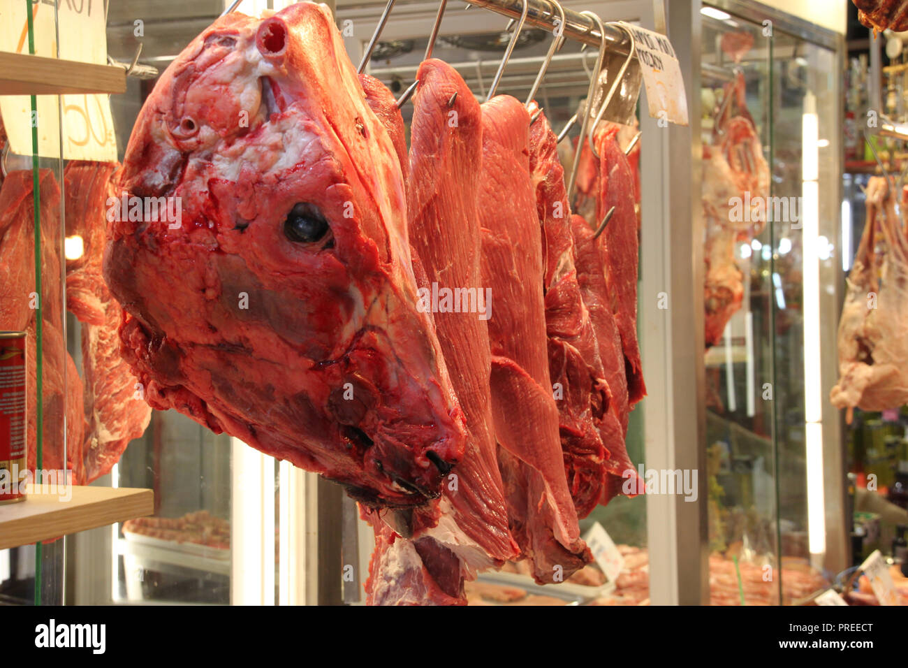 Tête de bœuf cru accroché sur boucherie parmi d'autres pièces de viande Banque D'Images