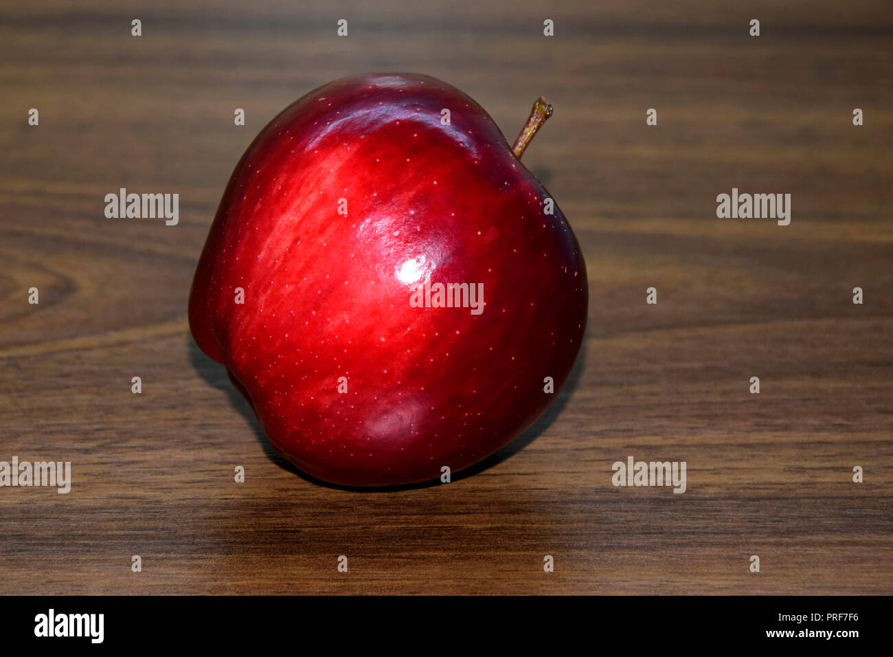 Un brillant, venu la pomme Red Delicious lain incliné sur le bureau en bois brun, close-up vue latérale. Banque D'Images