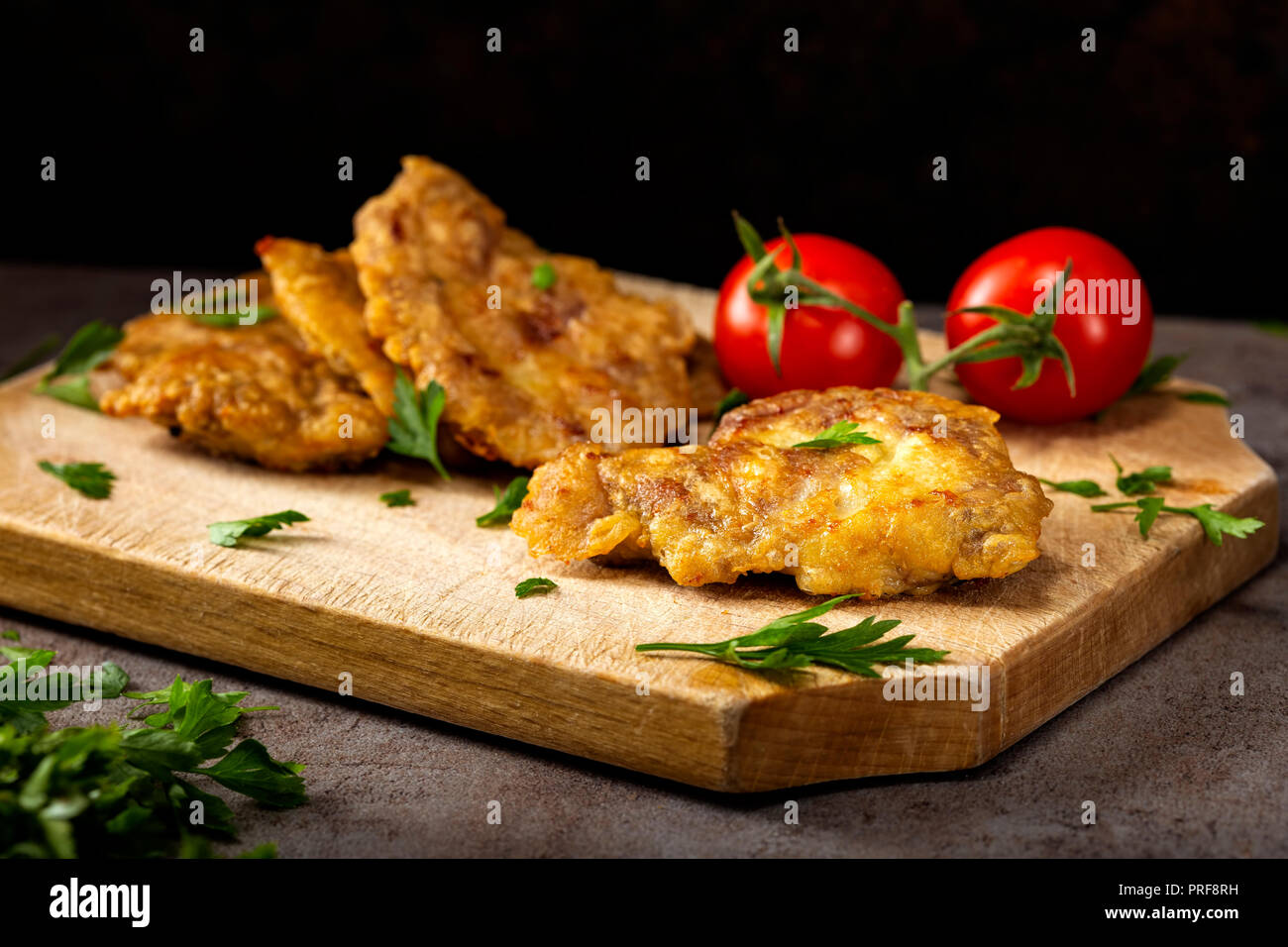 Escalope de porc de cerveau, la farine et les œufs sur une planche à découper en bois avec des herbes et des tomates Banque D'Images