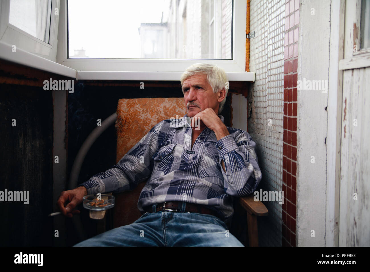 Portrait d'un homme aux cheveux gris à 60 ans. Un homme est assis sur une chaise et fume une cigarette Banque D'Images