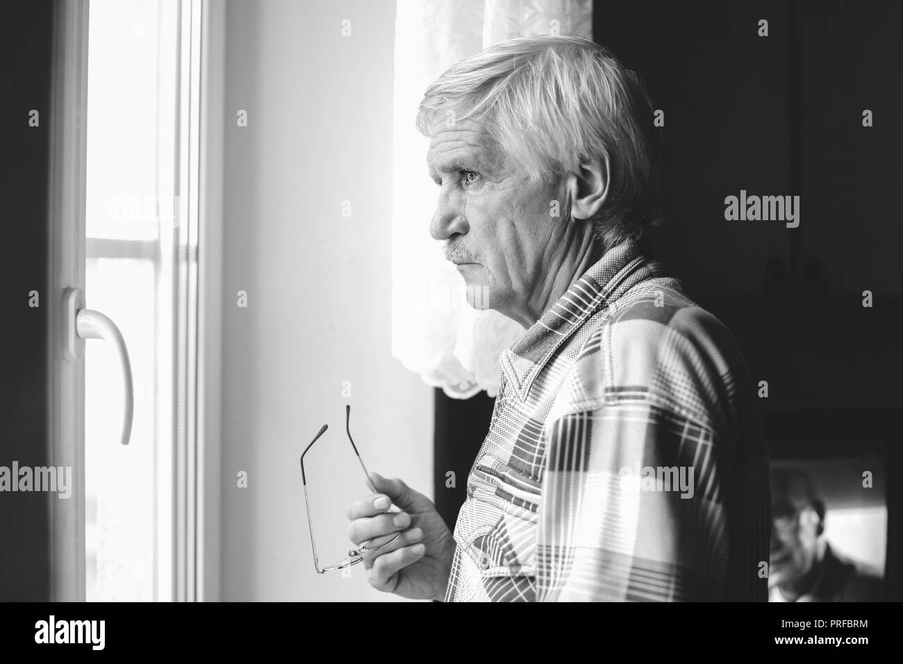 Portrait d'un homme aux cheveux gris à 60 ans. Un homme regarde par la fenêtre. L'homme a une mauvaise vision, il porte des lunettes Banque D'Images