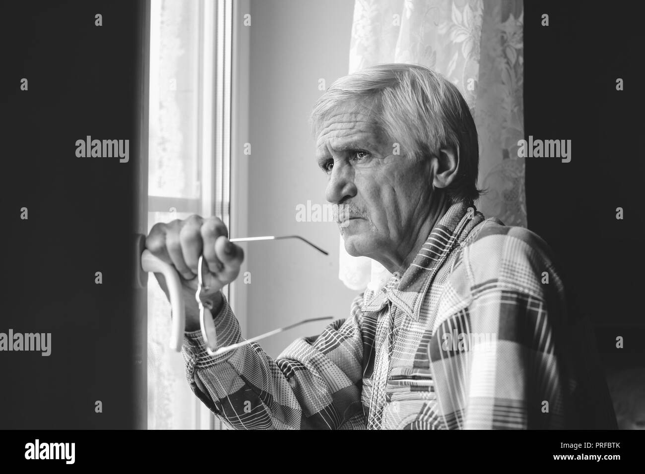 Portrait d'un homme aux cheveux gris à 60 ans. Un homme regarde par la fenêtre. L'homme a une mauvaise vision, il porte des lunettes Banque D'Images