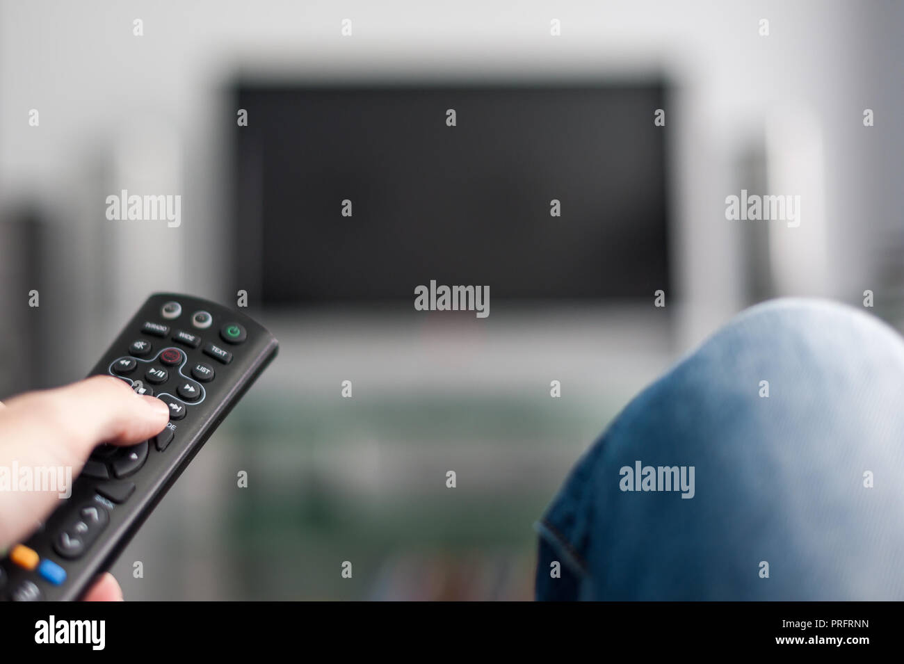 L'homme en jeans bleu sur la commutation d'une TV avec télécommande Banque D'Images