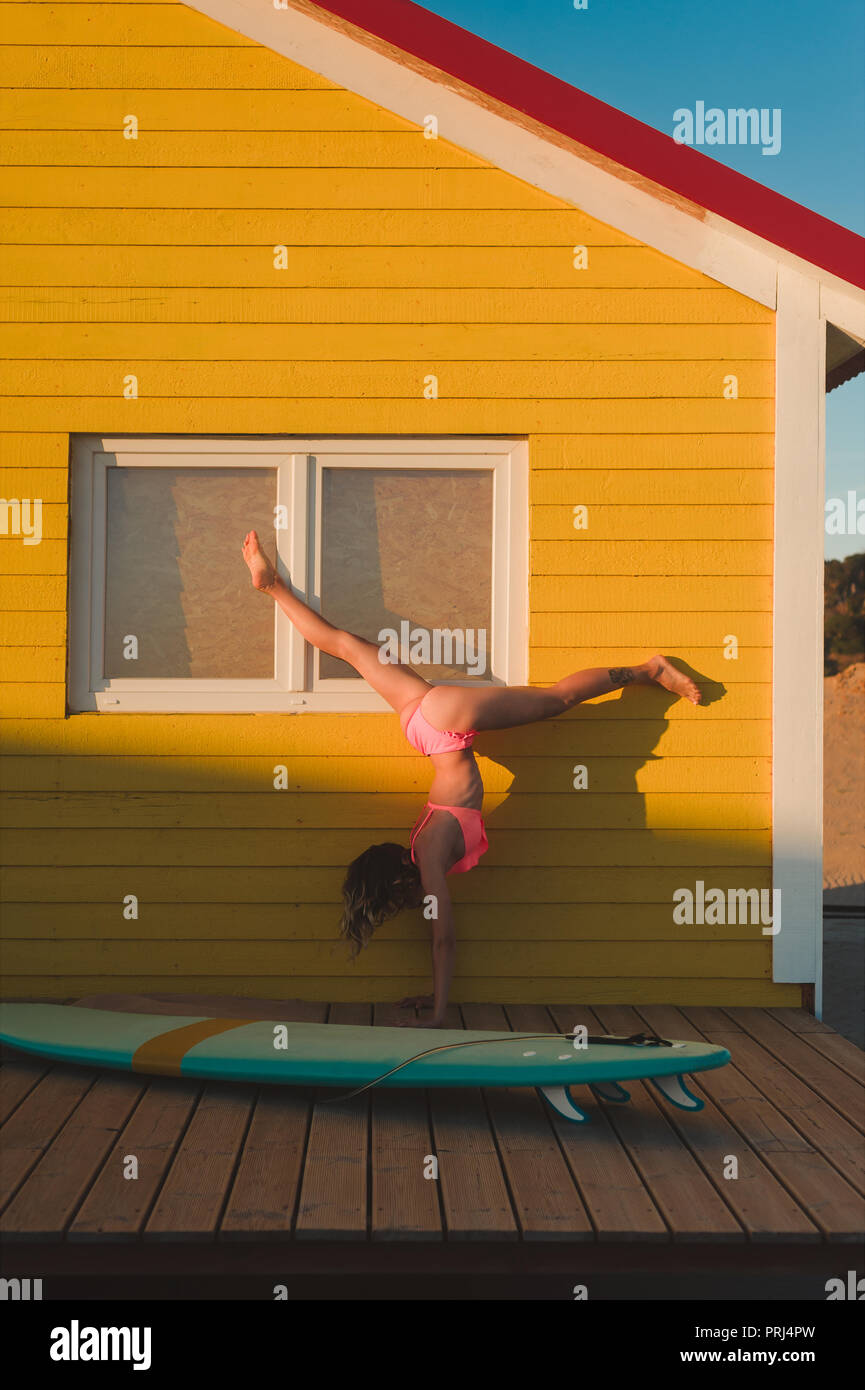 Young woman in pink bikini debout sur les mains contre bâtiment jaune avec voile à proximité au Portugal Banque D'Images