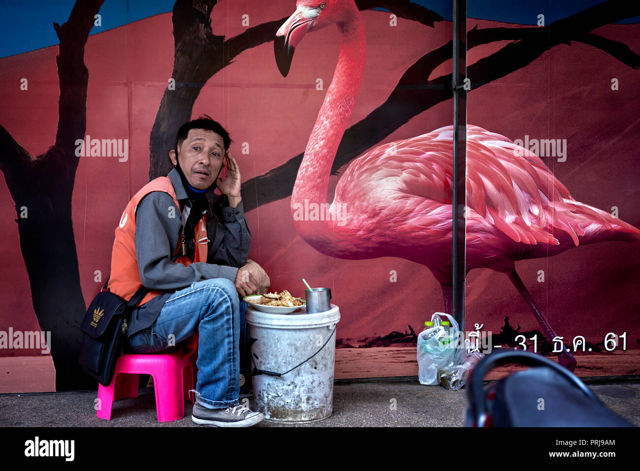 Décoration murale oiseau. Scène de rue en Thaïlande amusante avec un homme mangeant sur le trottoir avec un décor d'art mural de flamants d'animaux sauvages Banque D'Images