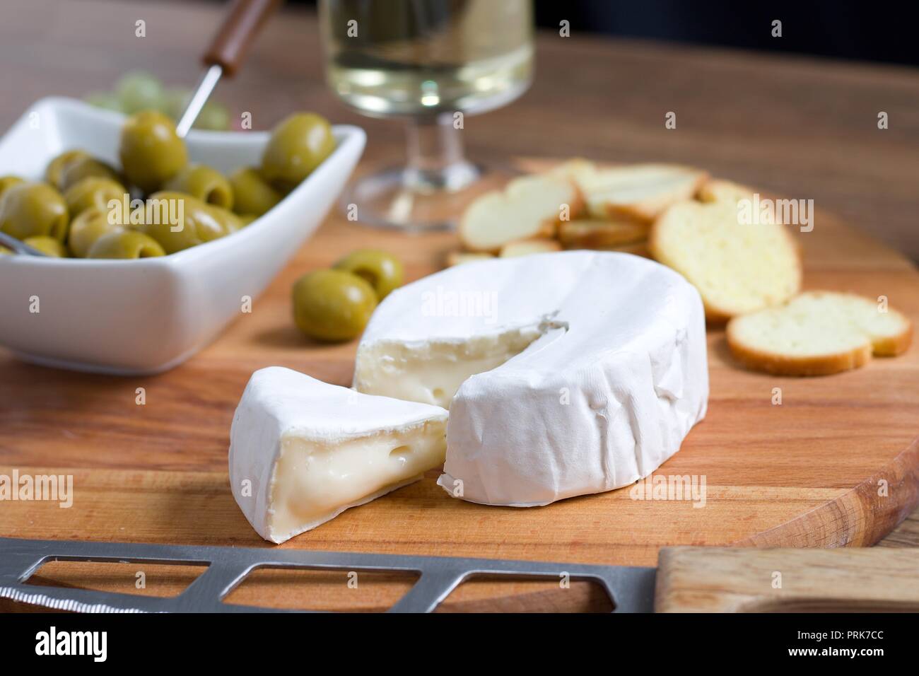 Fromage à pâte molle à croûte blanche (camembert ou brie) sur planche de bois avec des tranches de pain grillées, olives et vin blanc Banque D'Images