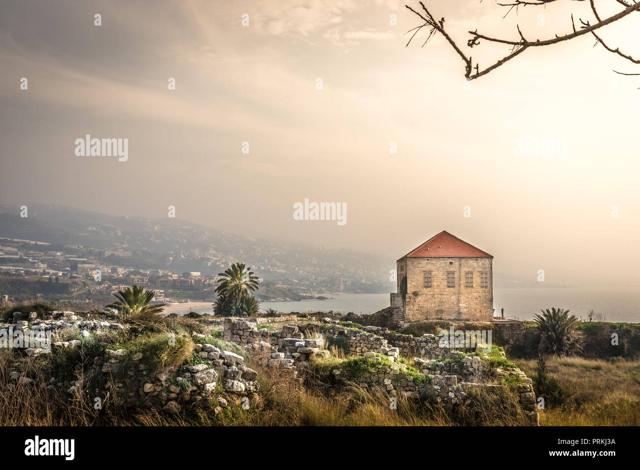 Vue paysage incroyable de Byblos, maison traditionnelle, rochers, palmiers, montagnes en arrière-plan. Haze lumière chaude au Liban Banque D'Images