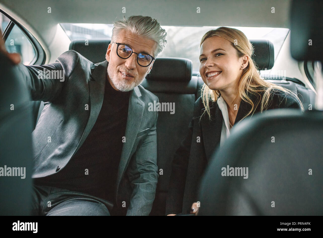 Senior businessman et son assistante assise dans la banquette arrière de la voiture et à la route en souriant. Les gens d'affaires voyageant en cabine. Banque D'Images
