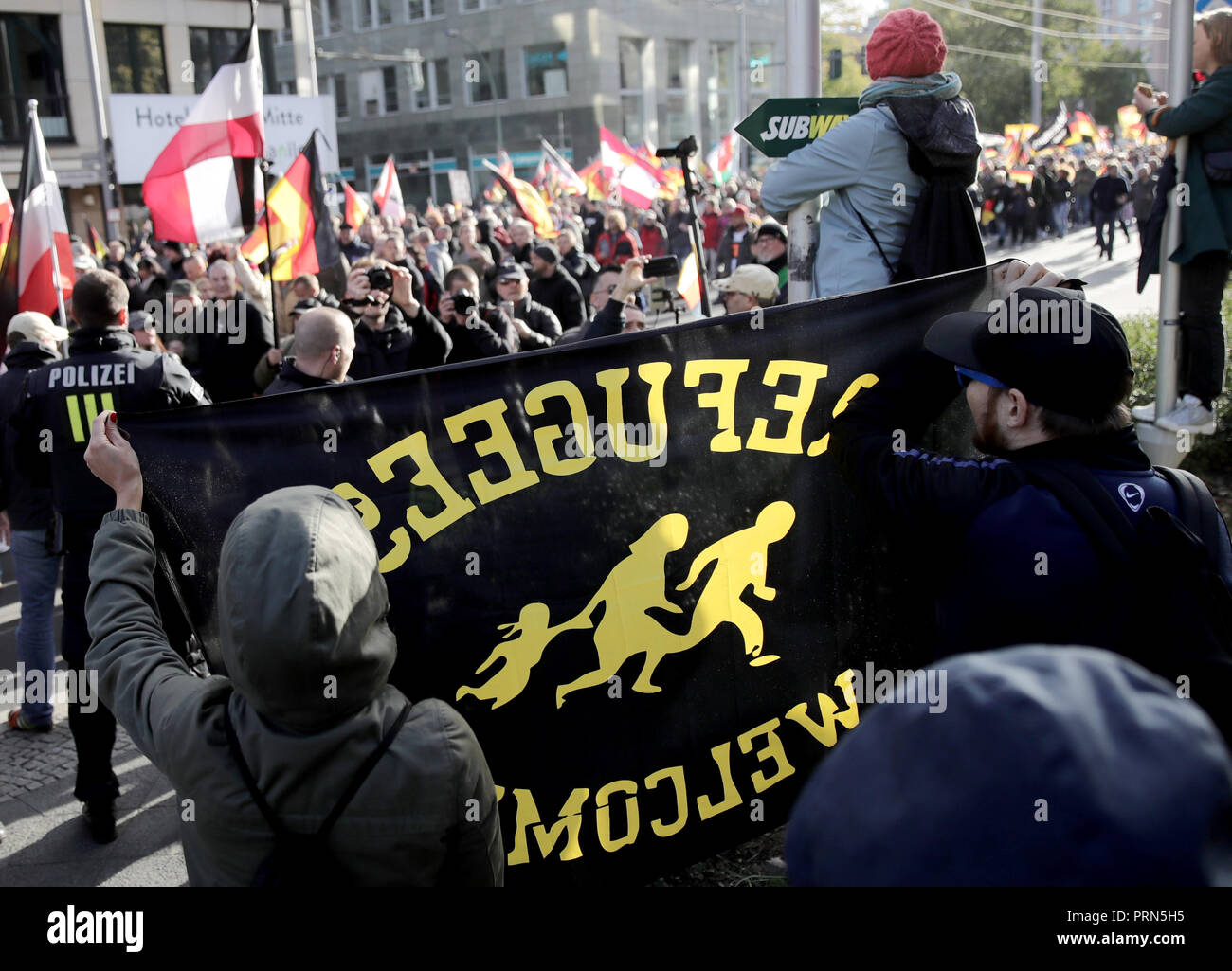 03 octobre 2018, Berlin : Au cours de la démonstration populiste de droite 'jour de la nation" de l'alliance pour l'Allemagne" "Nous avons une affiche avec l'inscription 'réfugiés bienvenue" peut être vu sur la route. Photo : Michael Kappeler/dpa Banque D'Images