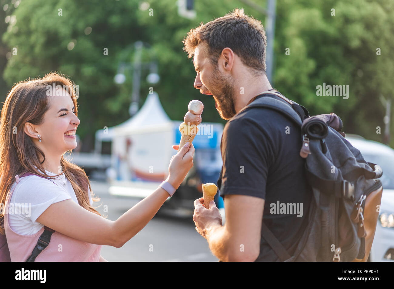 Happy young woman feeding petit ami aux yeux clos par la crème glacée à la rue en milieu urbain Banque D'Images