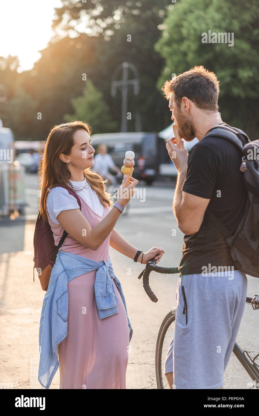 Jeune homme à la location la consommation de crème glacée pendant que sa petite amie, debout près de la rue à Banque D'Images
