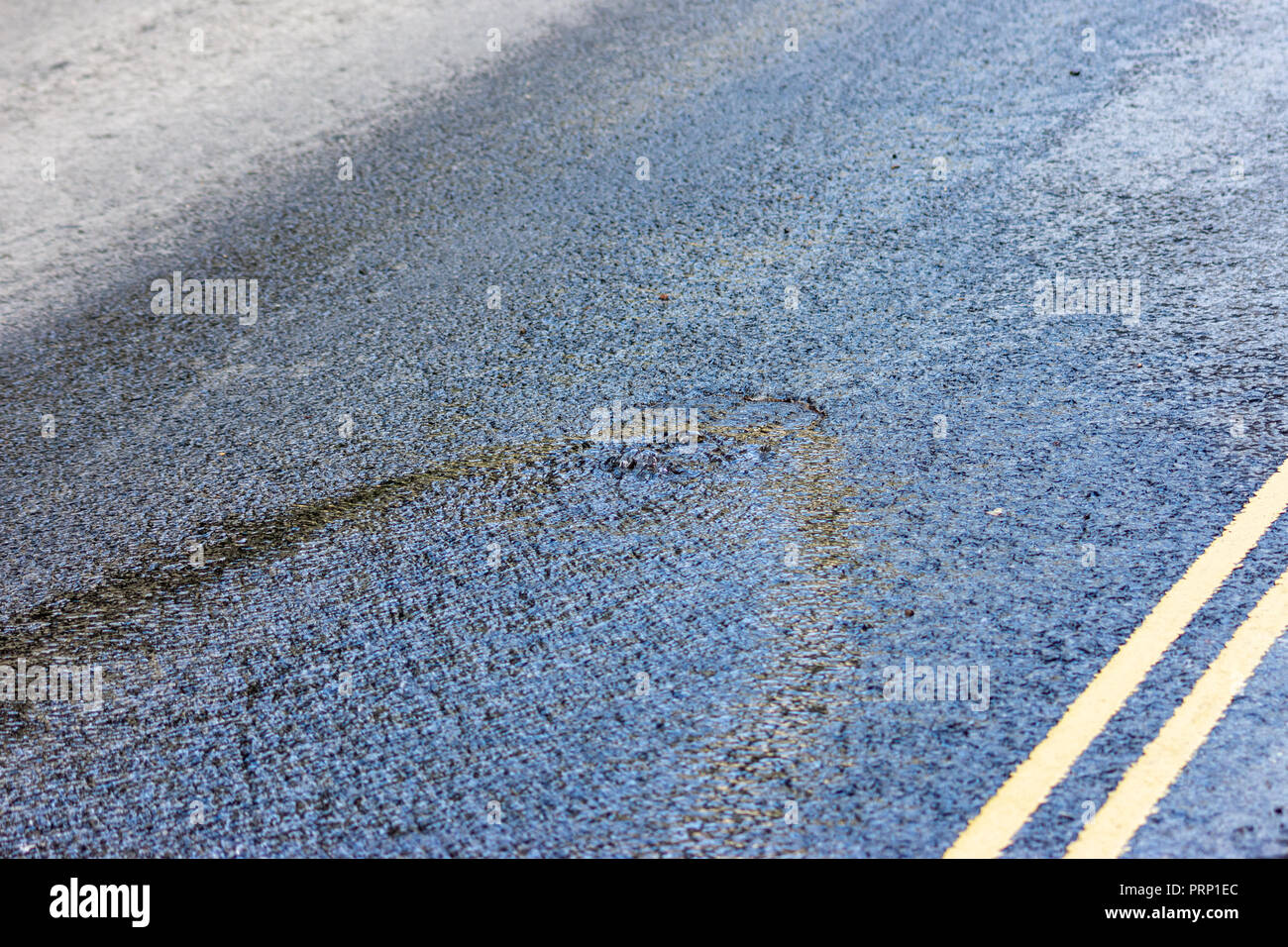 L'eau d'une rafale d'eau principale à venir par l'intermédiaire d'un couvercle de trou d'homme au milieu de la route Banque D'Images