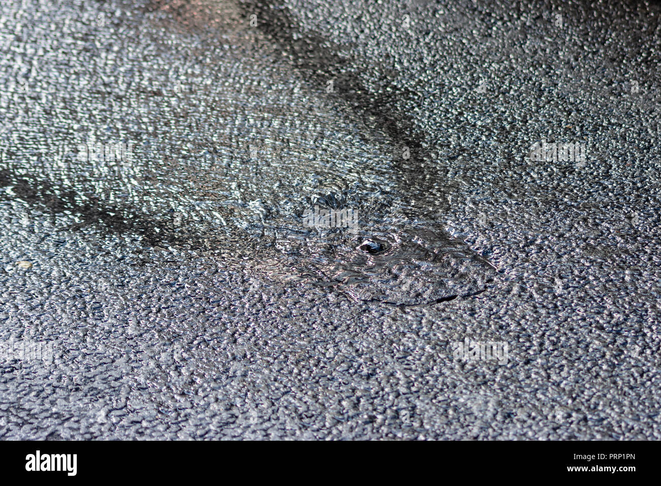 L'eau d'une rafale d'eau principale à venir par l'intermédiaire d'un couvercle de trou d'homme au milieu de la route Banque D'Images