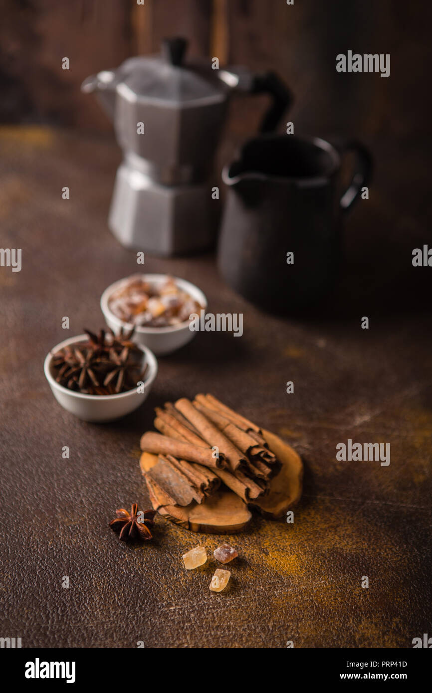 Les bâtons de cannelle, d'anis étoile, sucre caramélisé, cafetière et pot à lait sur fond sombre Banque D'Images