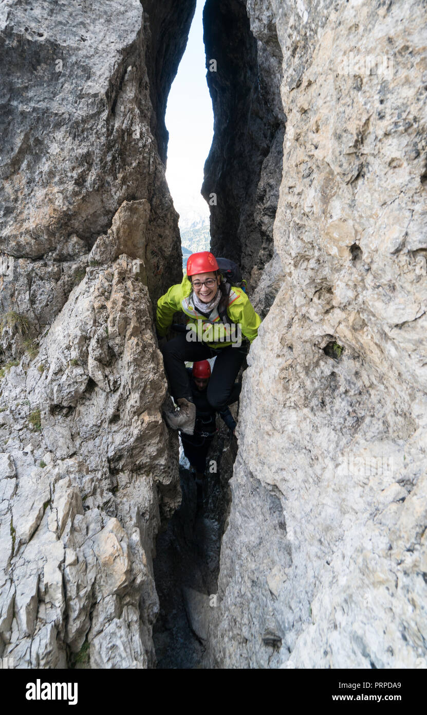 Deux jeunes femmes d'alpinistes passer par une étroite fissure sur une montée raide dans les Dolomites d'Alta Badia en Italie du nord Banque D'Images