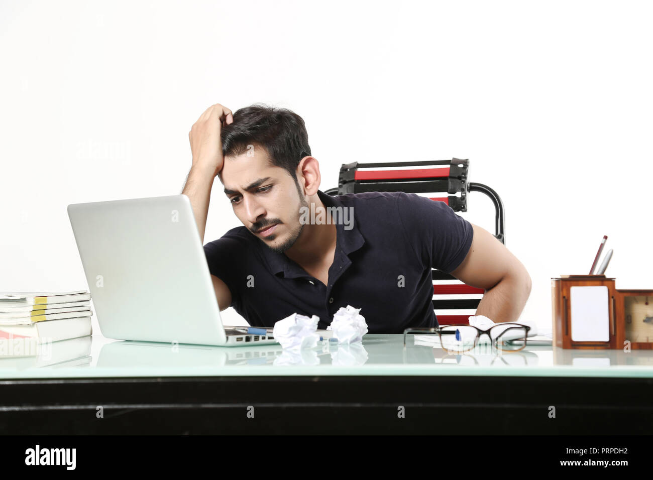 L'homme est à la recherche d'importants travaux de bureau sur un ordinateur portable avec des déchets de papier sur la table dans la cabine. Isolé sur fond blanc. Banque D'Images