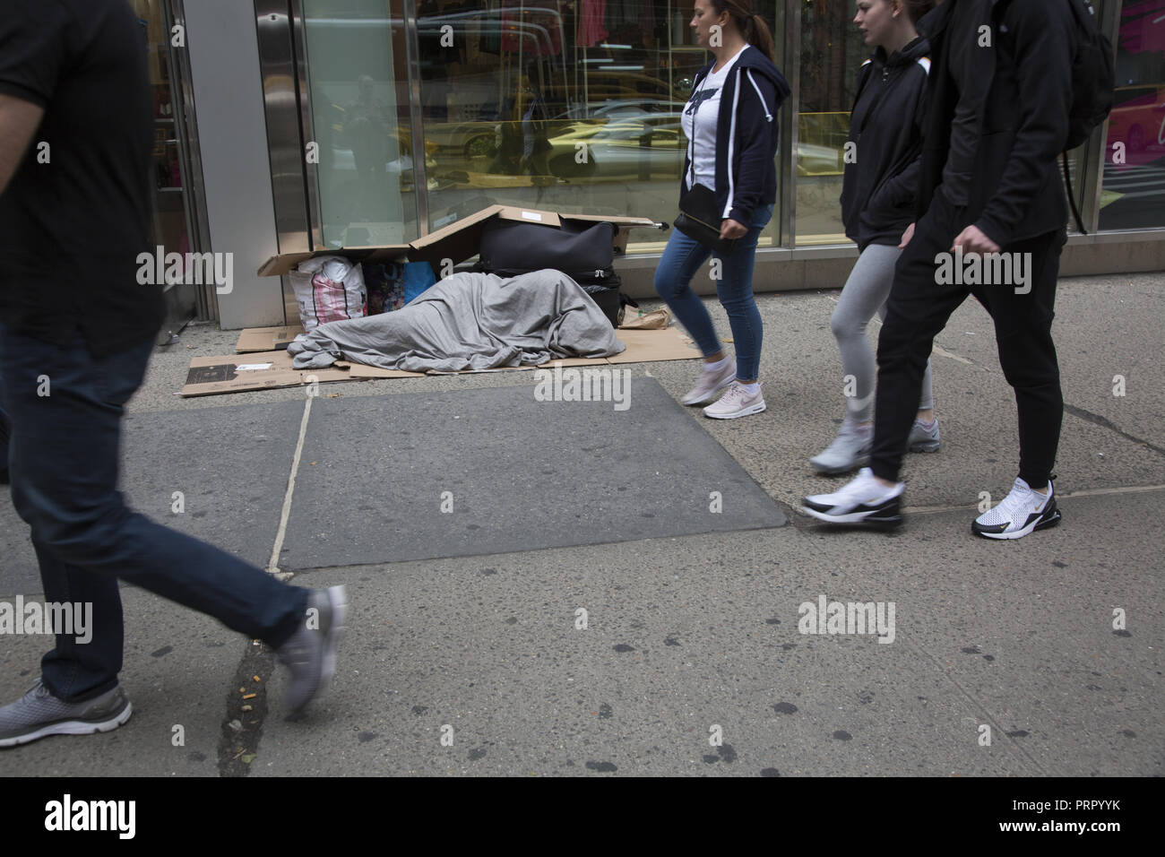 L'homme sans-abri dormir sur un trottoir au centre de Manhattan comme pedestr4ians par marche. Banque D'Images