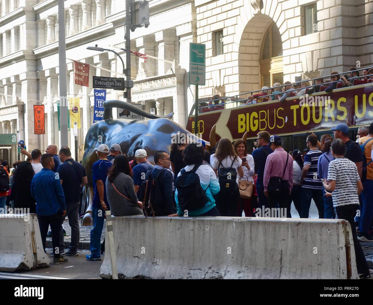 Les touristes de monde autour du Wall Street Bull charge alors que d'autres  vers le bas par les pairs d'un open top bus de tournée à Broadway, New York,  NY, USA Photo